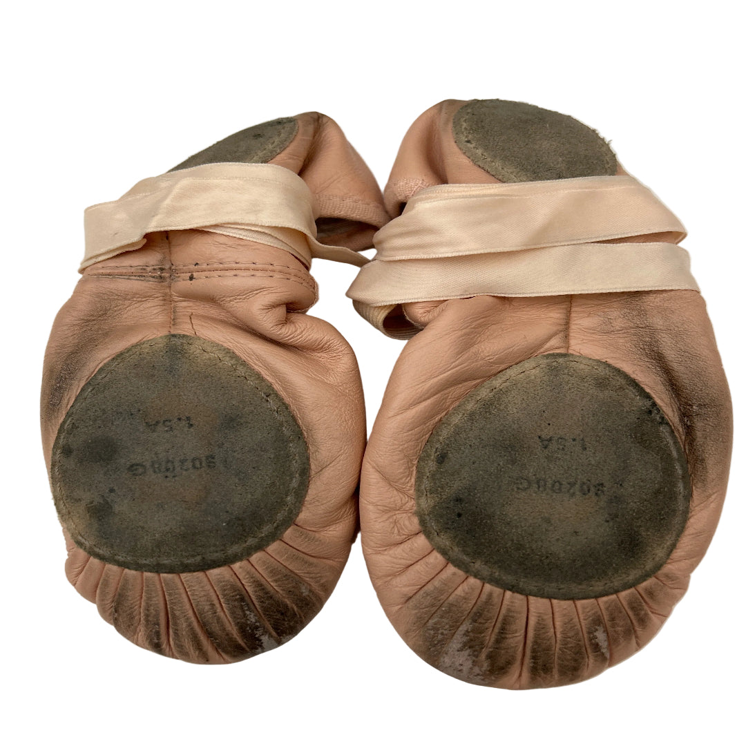 A pair of pink leather ballet shoes with  ribbons and suede soles, displayed on a white background.