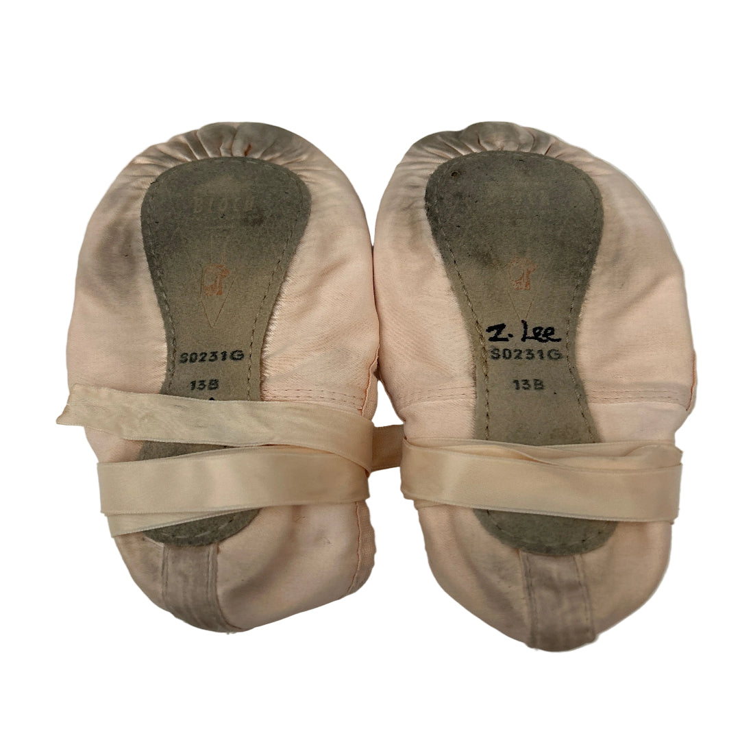 A pair of pink satin ballet shoes with ribbons, laid flat on a white background. 